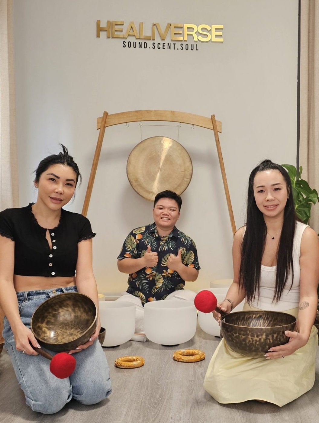 Kennedy giving a thumbs up between two guests holding singing bowls